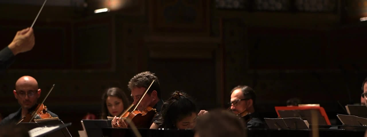 Sally Yapto at the piano, performing a concerto with a string orchestra behind her in a concert hall.