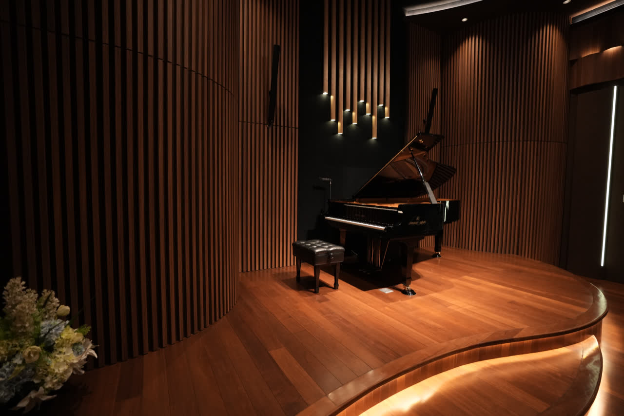 Piano konser Shigeru Kawai dengan tutup terbuka, di panggung kayu melengkung aula.